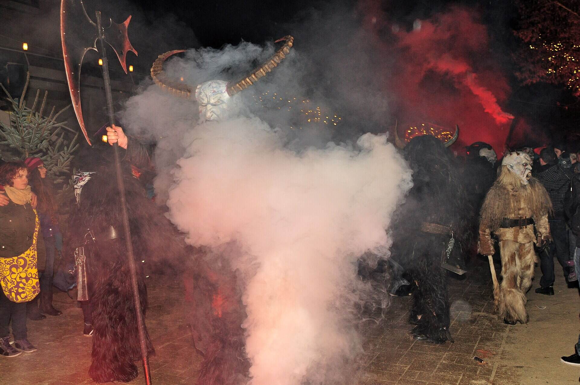 Krampusse mit Hörnern im roten Rauch beim Krampuslauf auf der Promenade in Pörtschach am Wörthersee in Kärnten