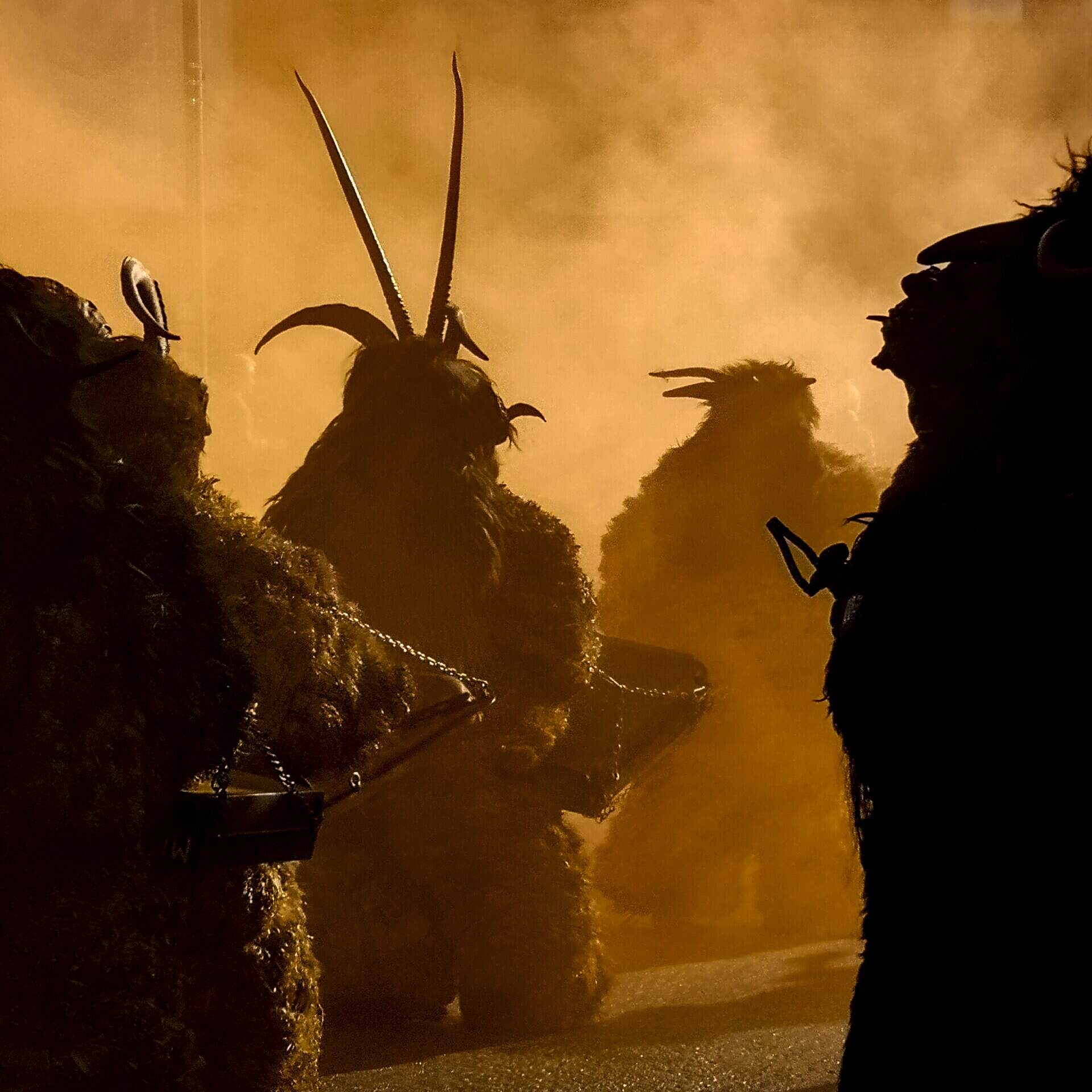 Krampusse mit Hörnern und Fell im farbigen Rauch beim Krampuslauf in Wiesing in Tirol