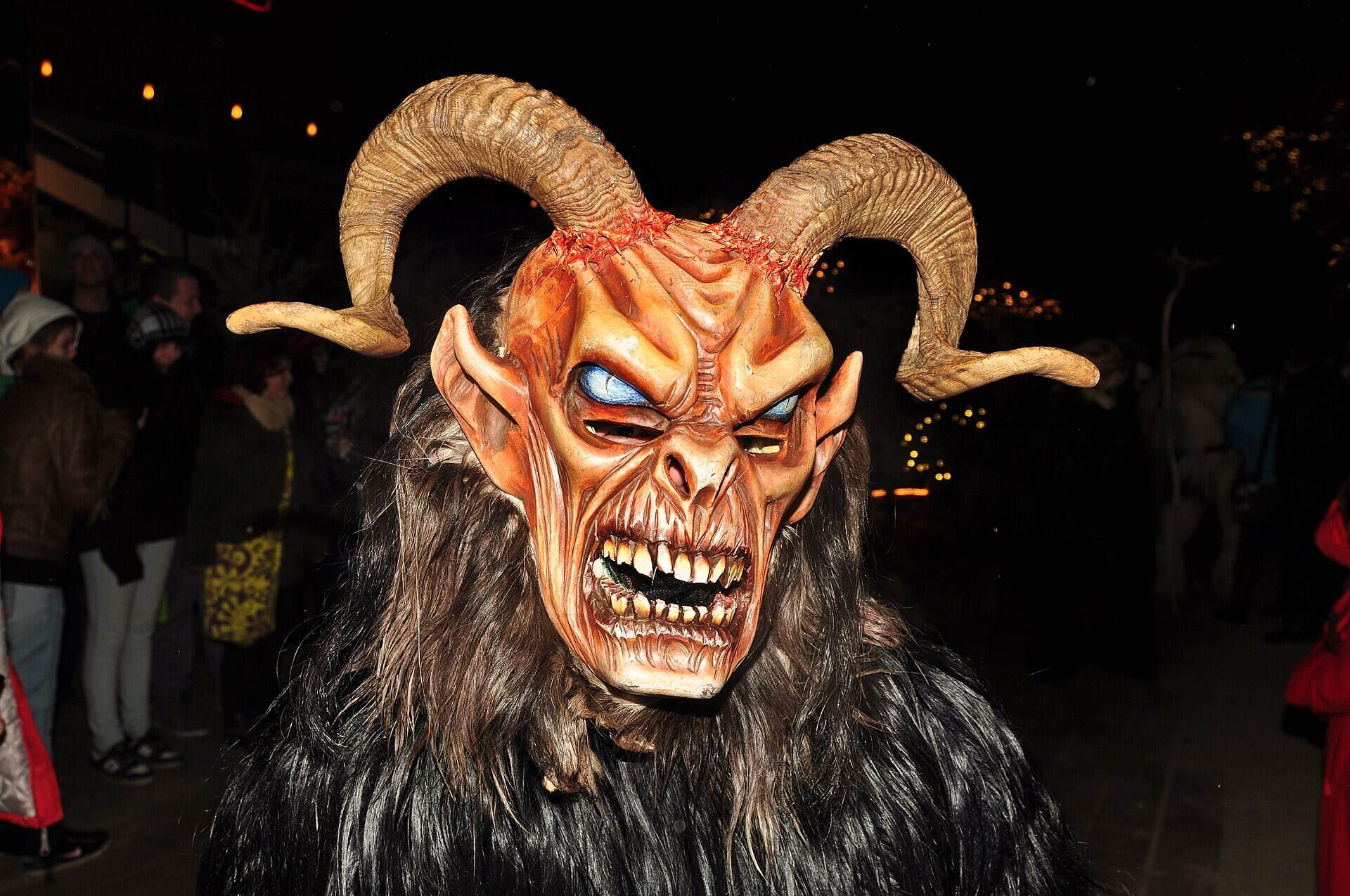 Handgeschnitzte Krampusmaske mit großen gedrehten Hörnern und Fell bei einem nächtlichen Krampuslauf