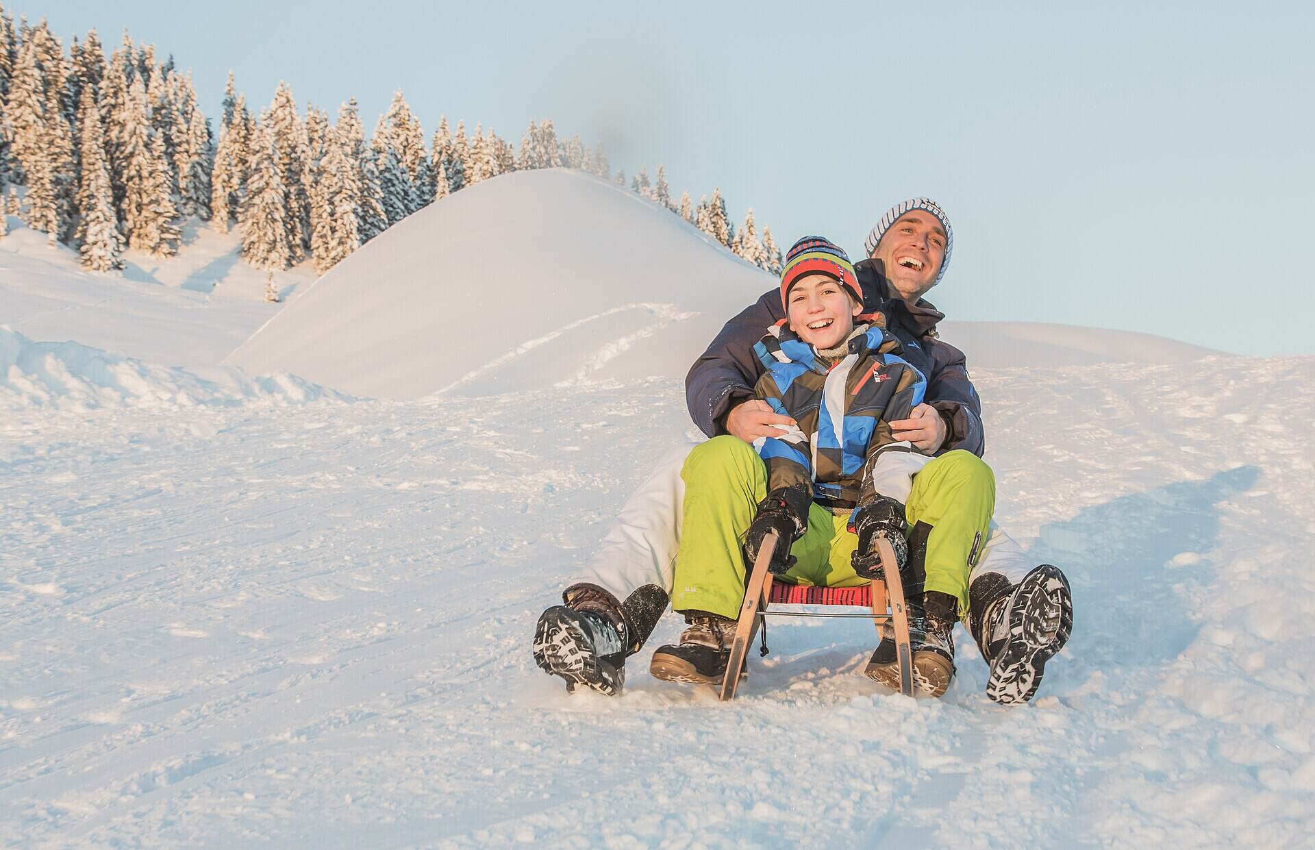 Vater und Kind fahren gemeinsam mit der Rodel durch den Schnee im Salzburger Land