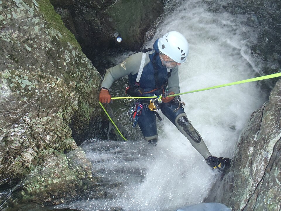 Person seilt sich neben einem Wasserfall in einer Schlucht ab